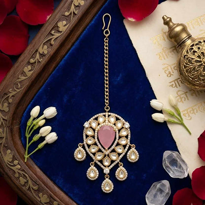Gold-plated bridal maang tikka with pink pear-shaped stone, Kundan-style teardrop crystals, and elegant dangling accents for weddings and festive wear.