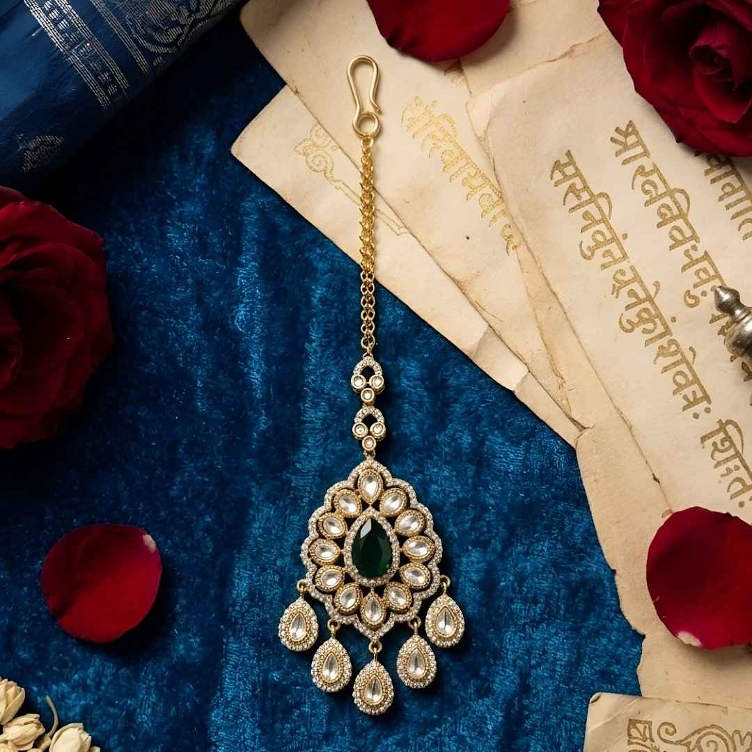 Gold-plated Kundan Maang Tikka with emerald green teardrop stone and white Kundan detailing for bridal and festive wear.