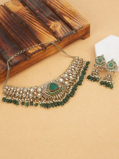 Detailed gold-toned statement necklace with intricate white stone embellishments and a prominent green teardrop centerpiece, finished with dangling green beads and pearls, paired with matching ornate drop earrings, displayed on a plain light background.