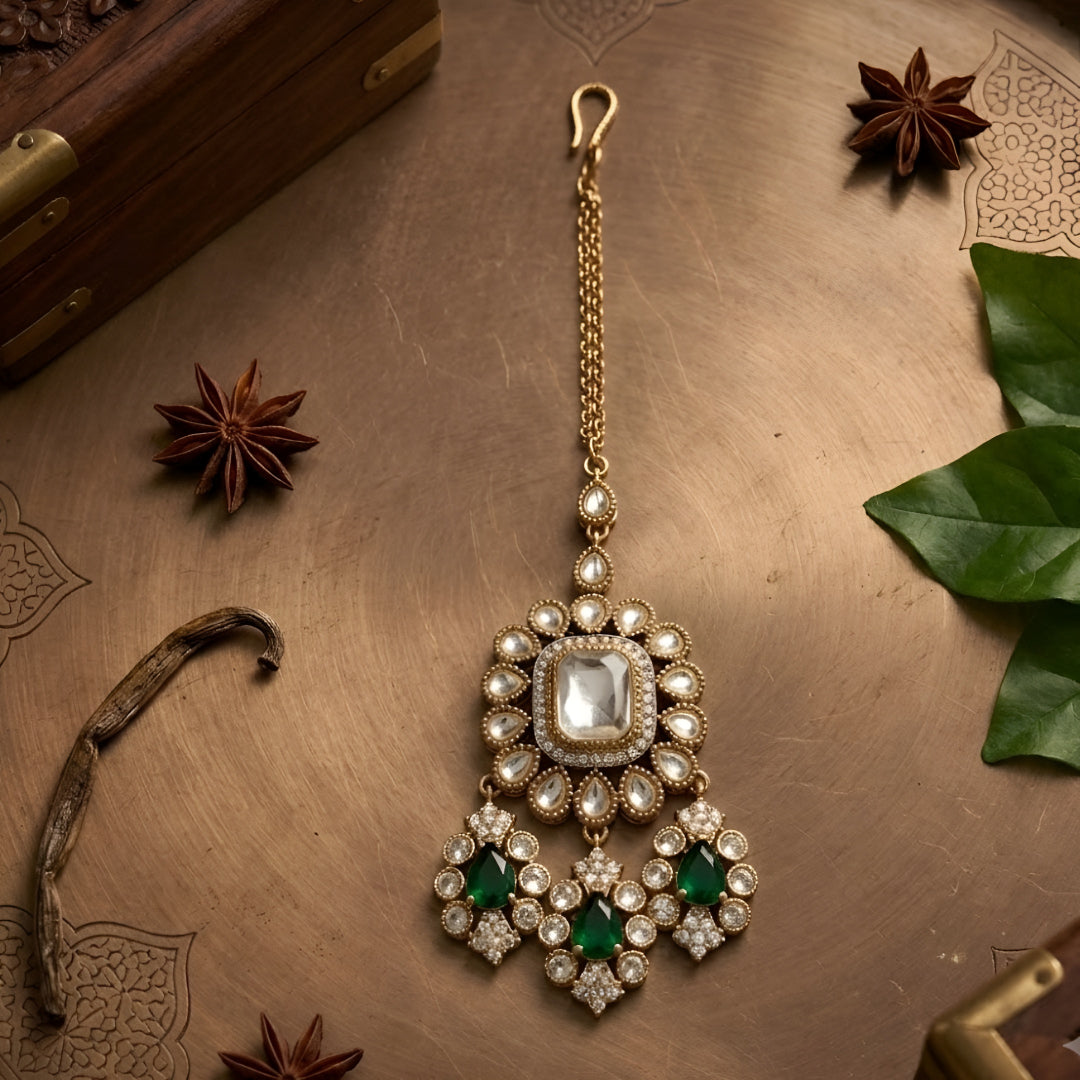 Gold-plated Kundan Maang Tikka featuring a square white center stone with emerald green teardrop stones and intricate floral detailing for bridal and festive wear.