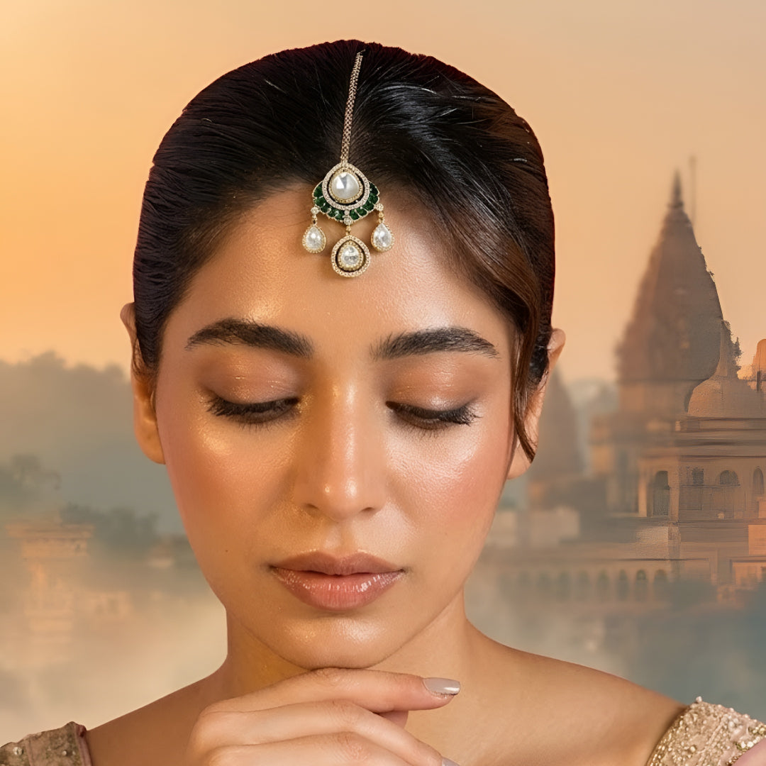 Gold-toned Kundan teardrop maang tikka with green stone detailing and three dangling teardrop charms for bridal and festive wear.
