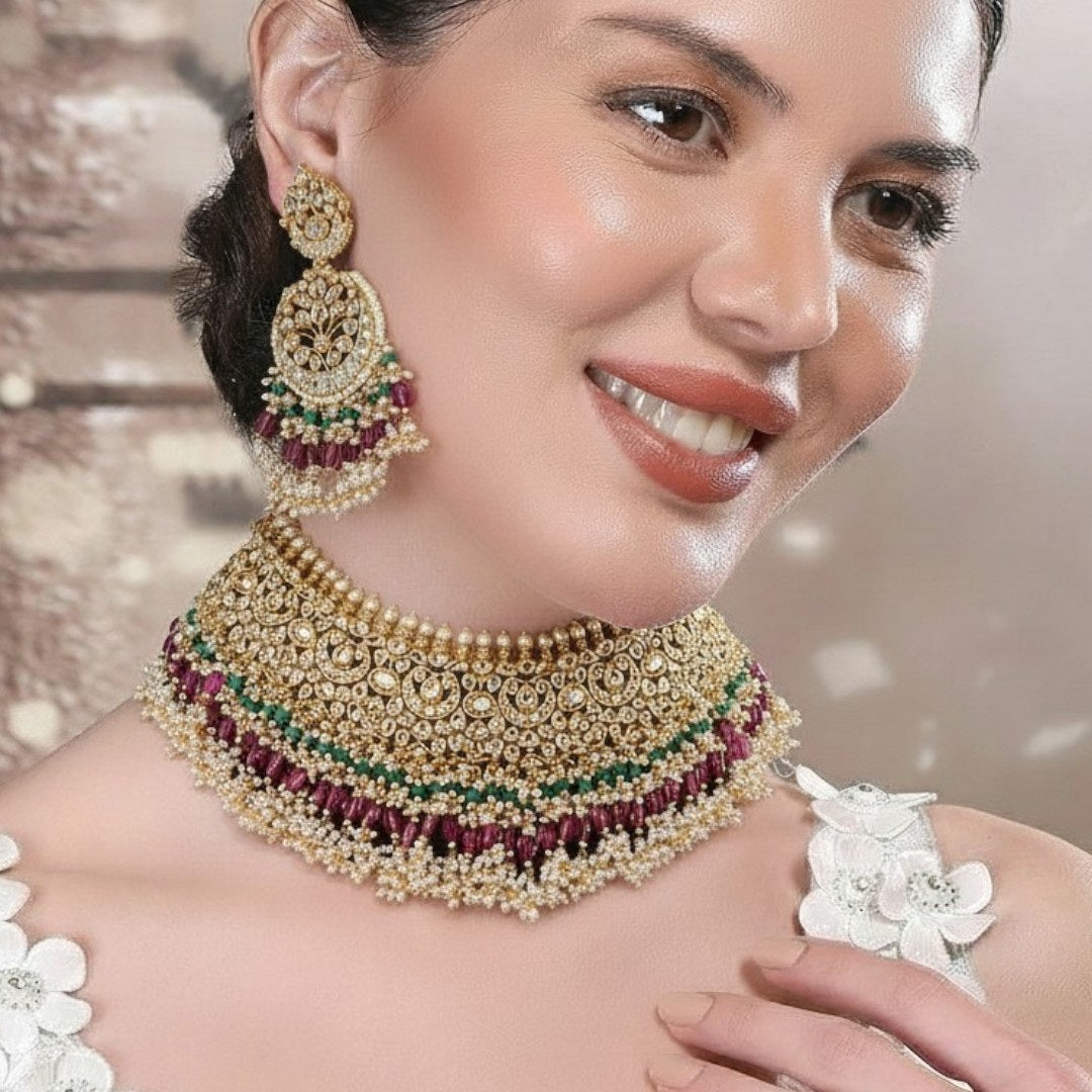 "Traditional gold-tone kundan bridal necklace set with ruby red and emerald green beads, paired with matching chandbali earrings on maroon silk background"