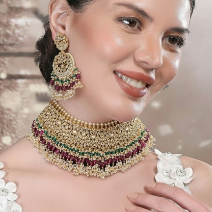 "Traditional gold-tone kundan bridal necklace set with ruby red and emerald green beads, paired with matching chandbali earrings on maroon silk background"