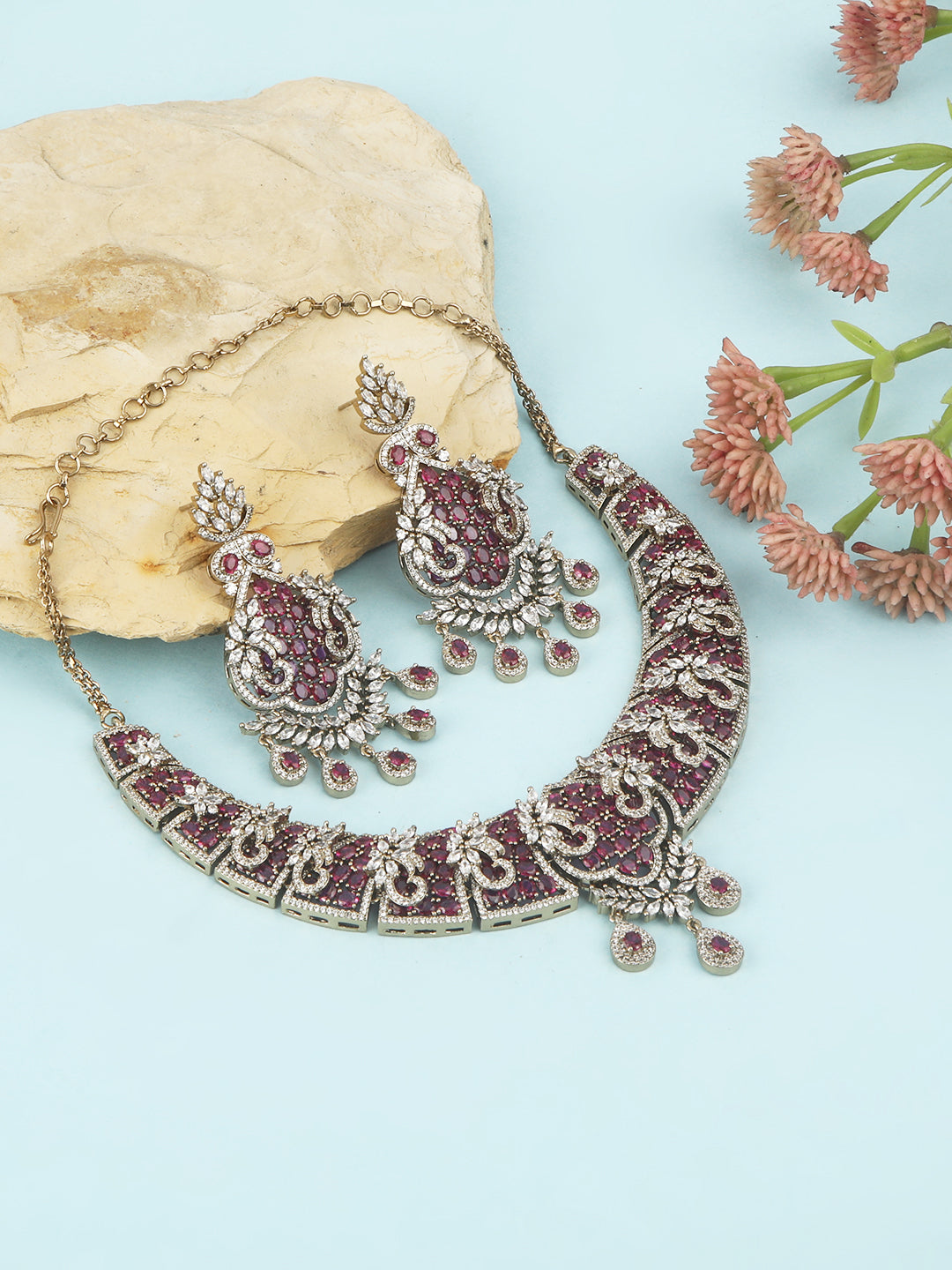 Gold-tone statement necklace set with pink ruby-style stones and clear crystals in an intricate floral design, paired with matching chandelier earrings featuring drop accents.
