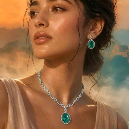 Silver-toned necklace set featuring an emerald green oval crystal pendant with matching drop earrings on a white background.