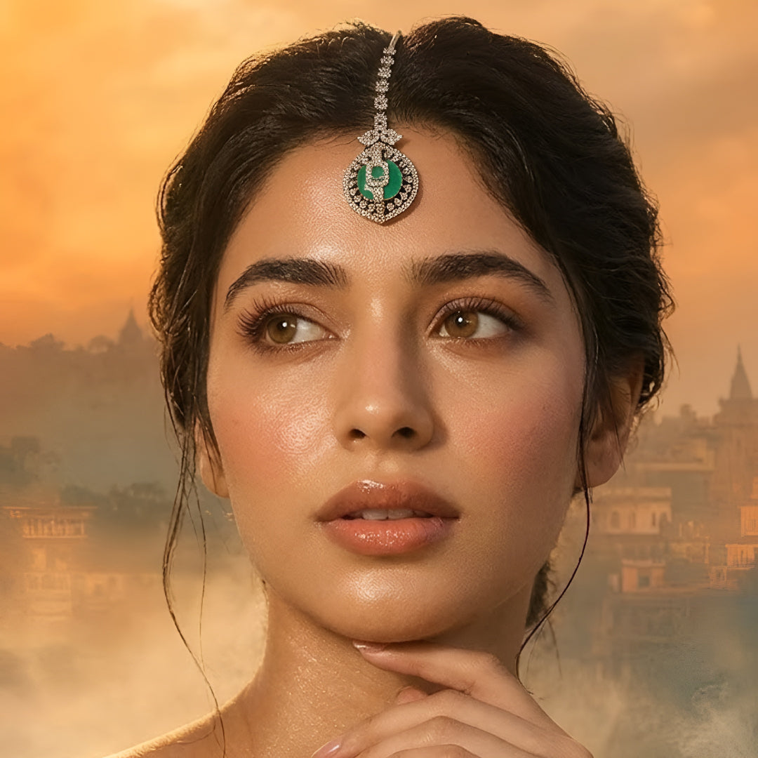 Gold-plated American Diamond maang tikka with an emerald-green center stone and circular pendant for bridal and festive wear.