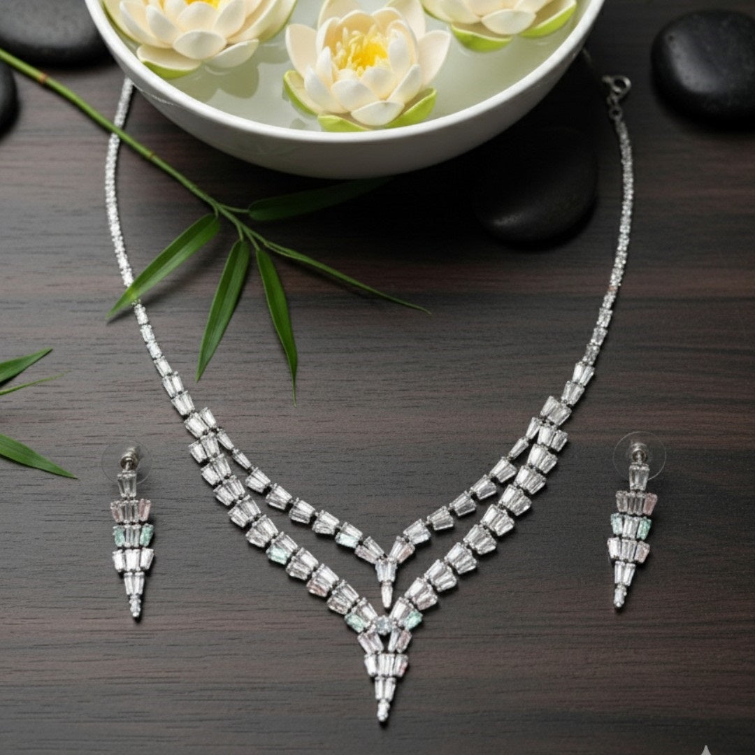 Elegant American Diamond necklace set displayed on a red velvet stand, featuring a double-layered V-shaped necklace with matching earrings, perfect for bridal or party wear.