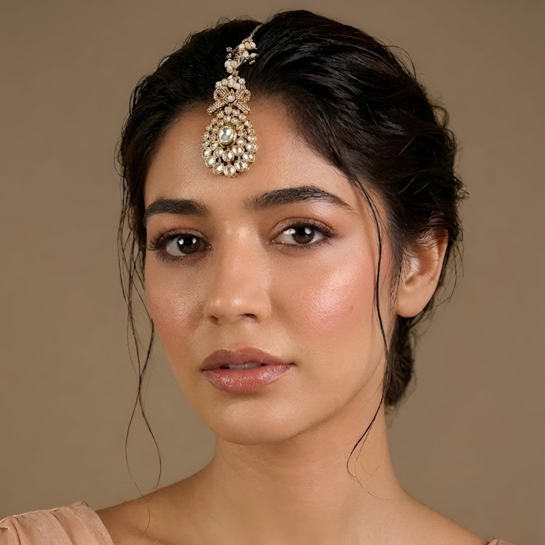 Gold-plated Kundan maang tikka with sparkling clear stones, pearl bead drops, and an elegant bridal design for weddings and festive wear.