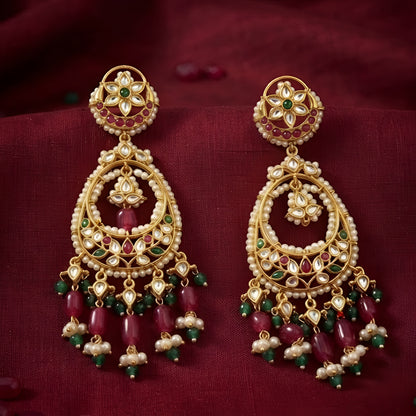 Antique gold Kundan Chandbali earrings with ruby and green stones, pearl border, and elegant bead danglers for women.