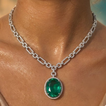 Silver-toned necklace set featuring an emerald green oval crystal pendant with matching drop earrings on a white background.