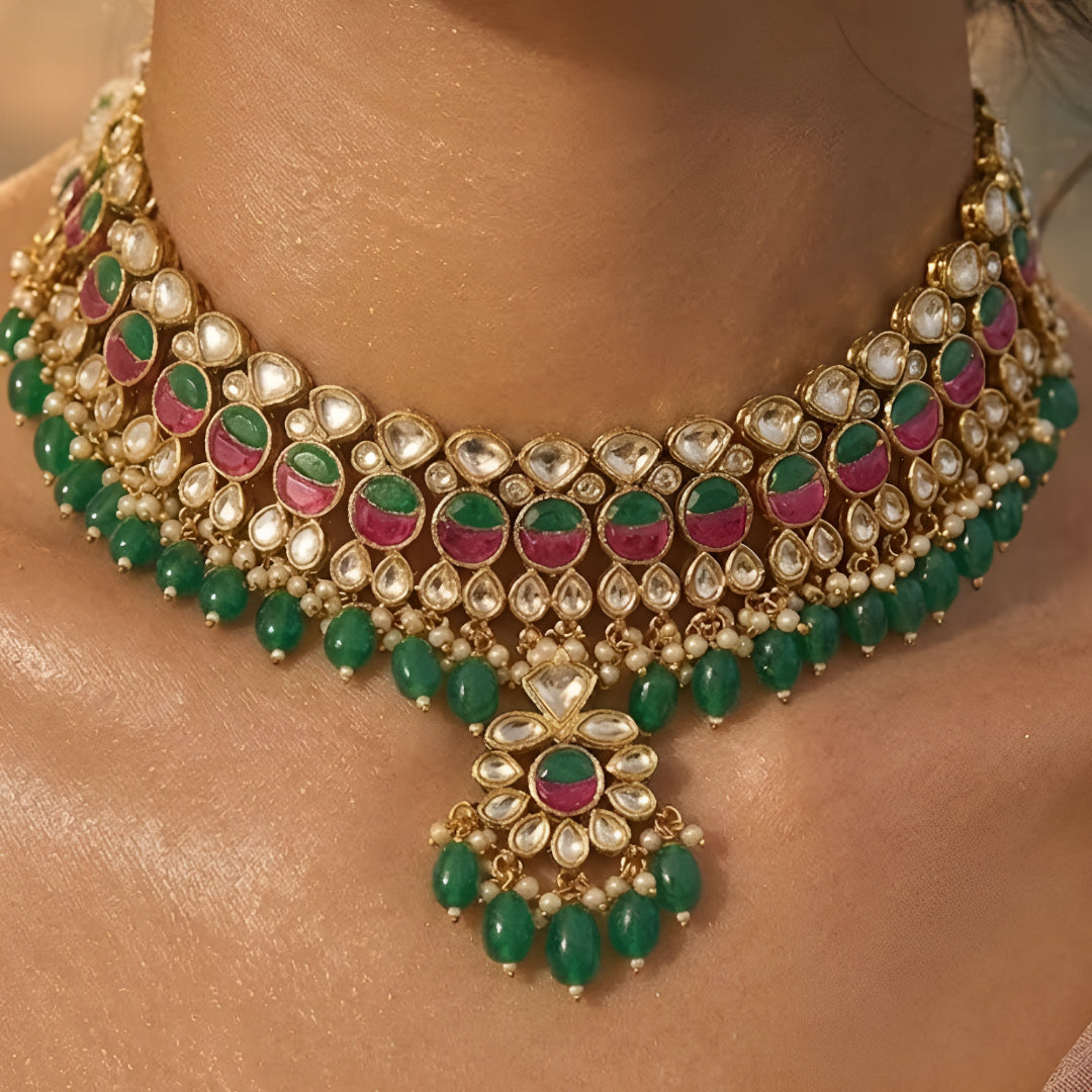 Traditional Kundan choker necklace set with pink stone detailing, green bead drops, and matching earrings in gold-plated finish for bridal wear.