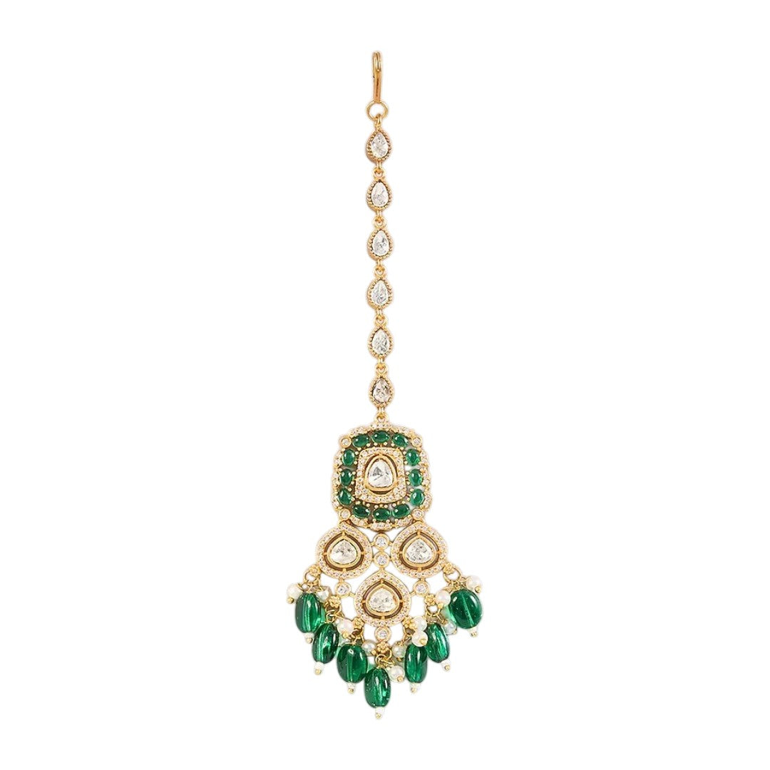 Gold-toned Kundan maang tikka with green stones, teardrop crystals, pearl accents, and dangling green beads for bridal and festive wear.