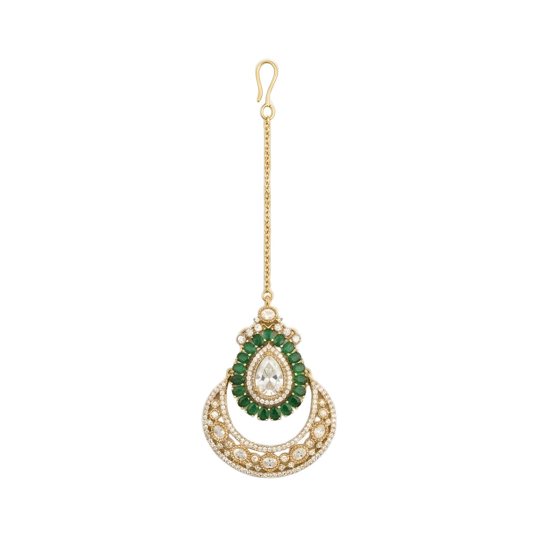 Elegant gold-plated bridal maang tikka featuring a pear-shaped crystal, green stones, and crescent crystal design for weddings and festive occasions.