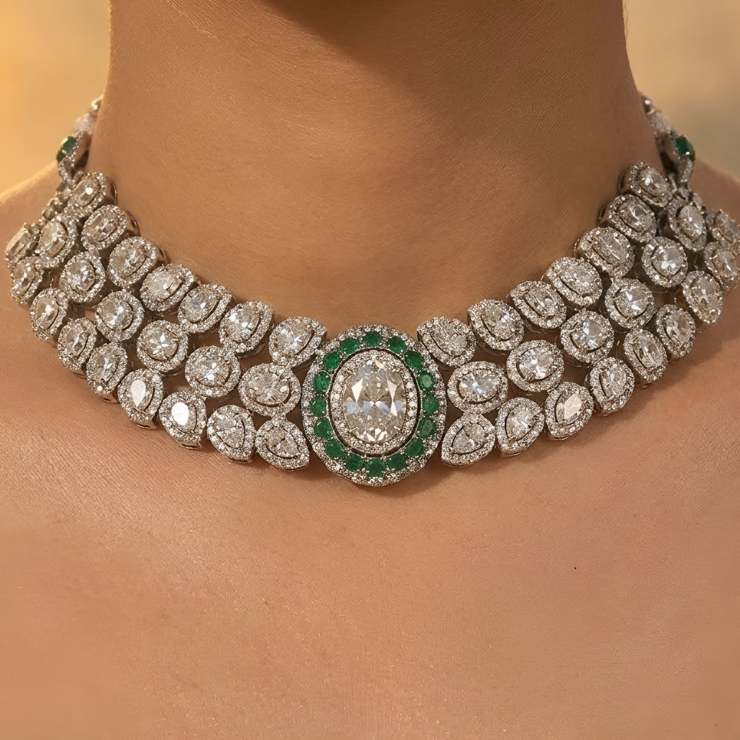 Elegant diamond and emerald choker necklace set with matching stud earrings featuring intricate floral motifs, sparkling white stones, green gemstone accents, and a luxurious gold-tone finish.
