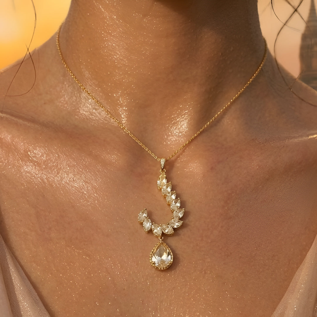 Gold-toned leaf design pendant necklace set with teardrop crystal pendant and matching drop earrings on a white background.