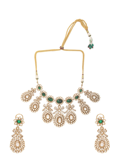 Gold-toned necklace with a braided cord and adjustable tassel tie, featuring intricate white stone detailing with oval green gemstones and multiple dangling teardrop motifs, paired with matching drop earrings, displayed on a plain light background.