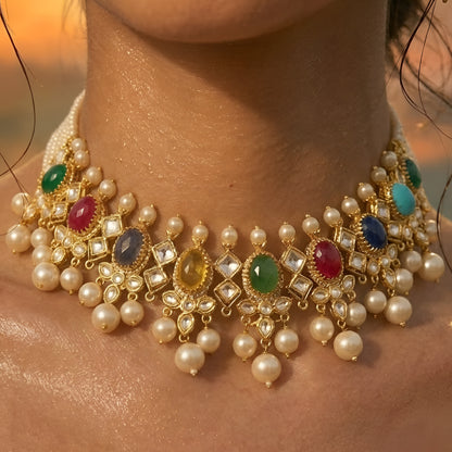 Gold-toned Navratna Kundan choker necklace set with multicolored stones, pearl drops, and matching green stone jhumka earrings on a white background.