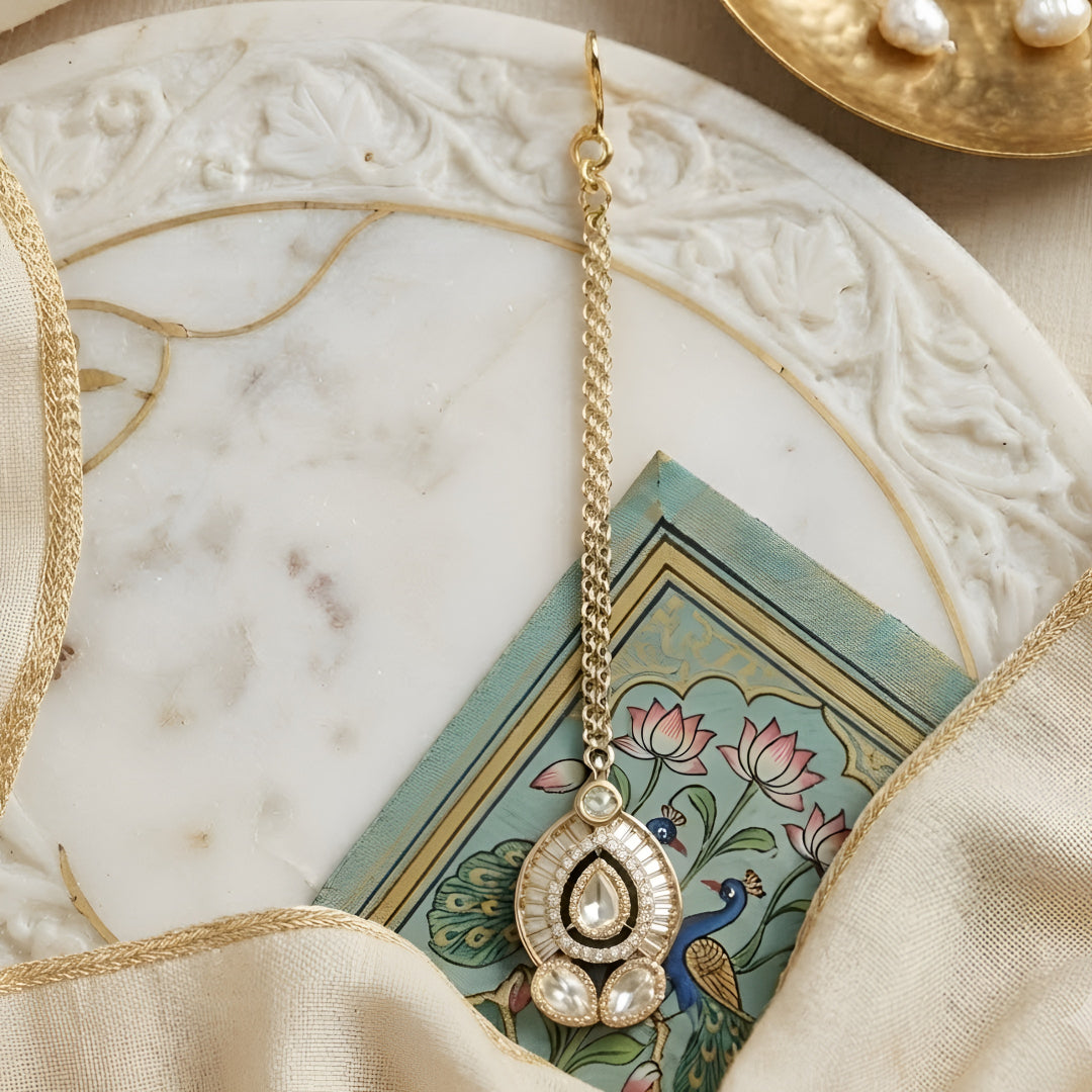 Elegant gold-plated Kundan pearl maang tikka with teardrop stone and crystal detailing for bridal and festive wear.