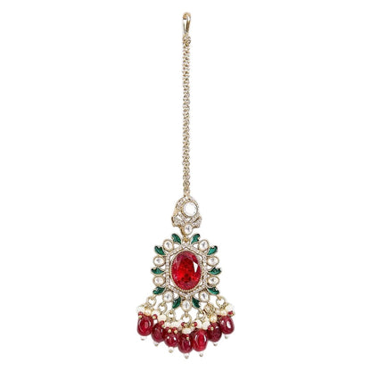 Gold-toned Kundan maang tikka with ruby red oval stone, green enamel detailing, sparkling Kundan stones, and red bead drops for bridal and festive wear.