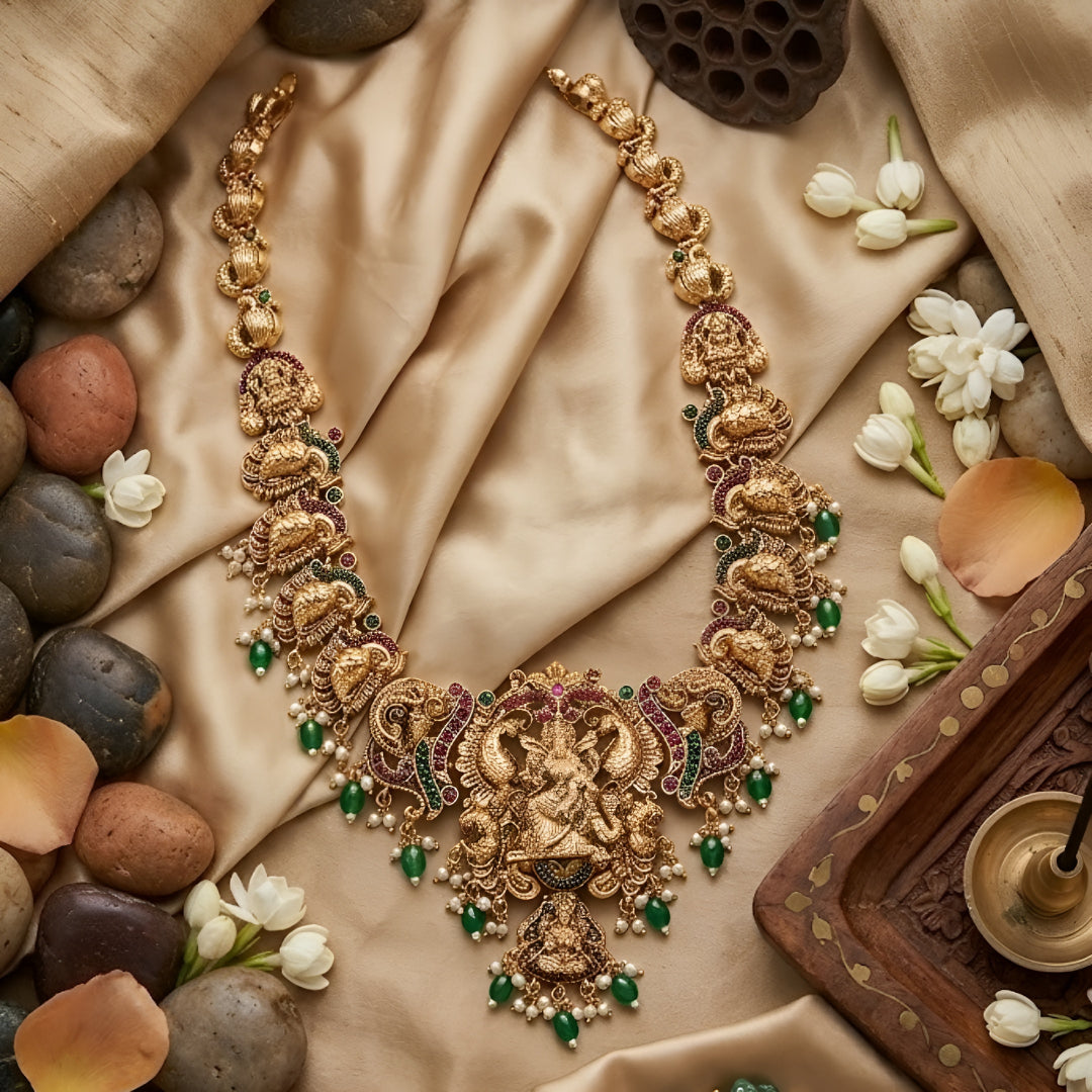 Antique gold Lakshmi temple necklace featuring traditional South Indian craftsmanship, ruby and green stone detailing, intricate deity motifs, and green bead drops for bridal and festive occasions.