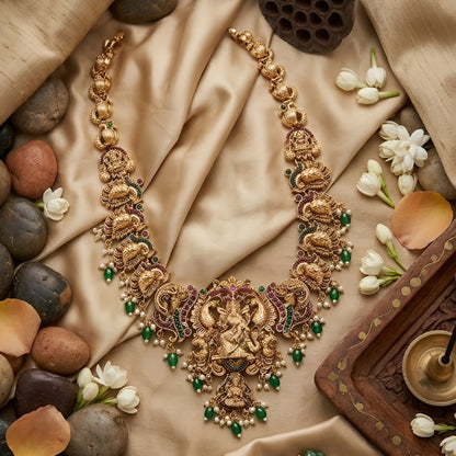 Antique gold Lakshmi temple necklace featuring traditional South Indian craftsmanship, ruby and green stone detailing, intricate deity motifs, and green bead drops for bridal and festive occasions.