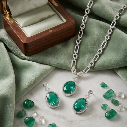 Silver-toned necklace set featuring an emerald green oval crystal pendant with matching drop earrings on a white background.