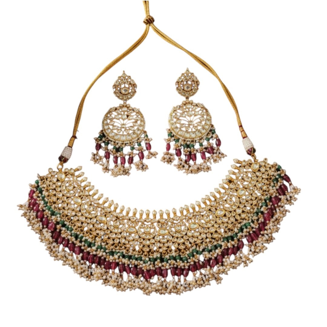 "Traditional gold-tone kundan bridal necklace set with ruby red and emerald green beads, paired with matching chandbali earrings on maroon silk background"
