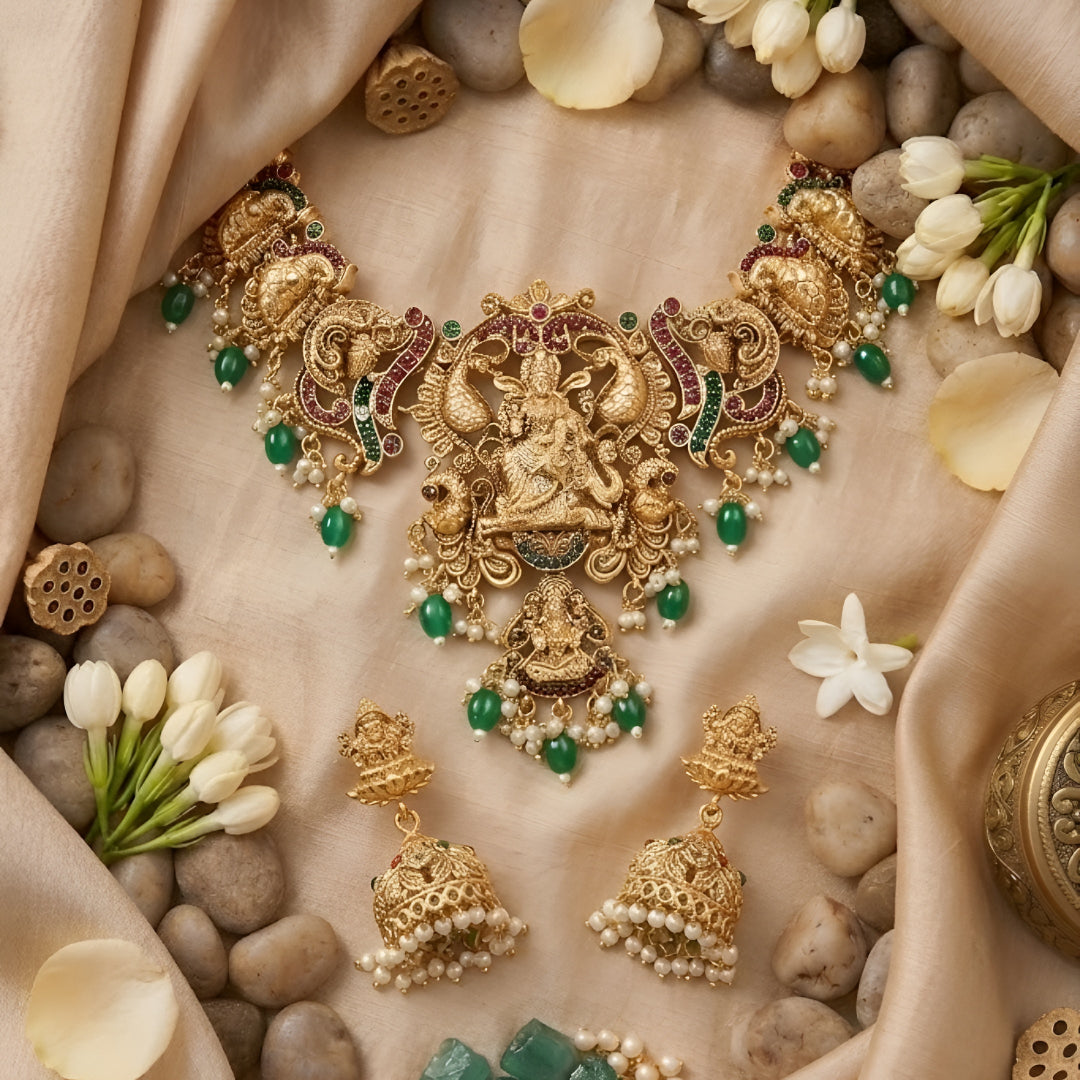 Traditional South Indian Temple Jewellery Lakshmi Necklace Set with matching Jhumka Earrings, antique gold finish, green bead drops, and ruby stone embellishments for bridal and festive wear.