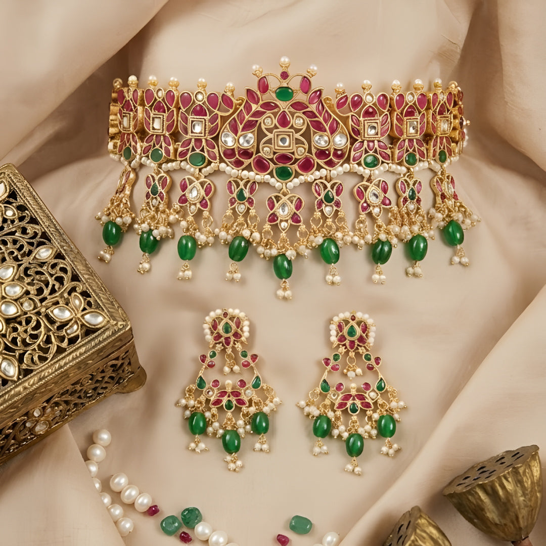 Traditional gold-plated Kundan choker necklace set with red and green stones, dangling green beads, and matching chandbali earrings for bridal wear.