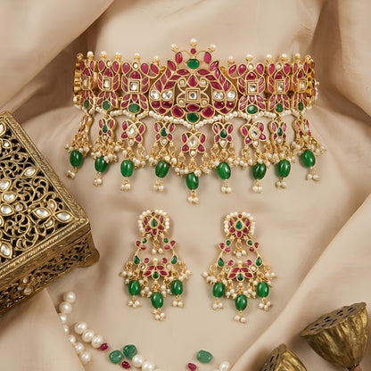Traditional gold-plated Kundan choker necklace set with red and green stones, dangling green beads, and matching chandbali earrings for bridal wear.