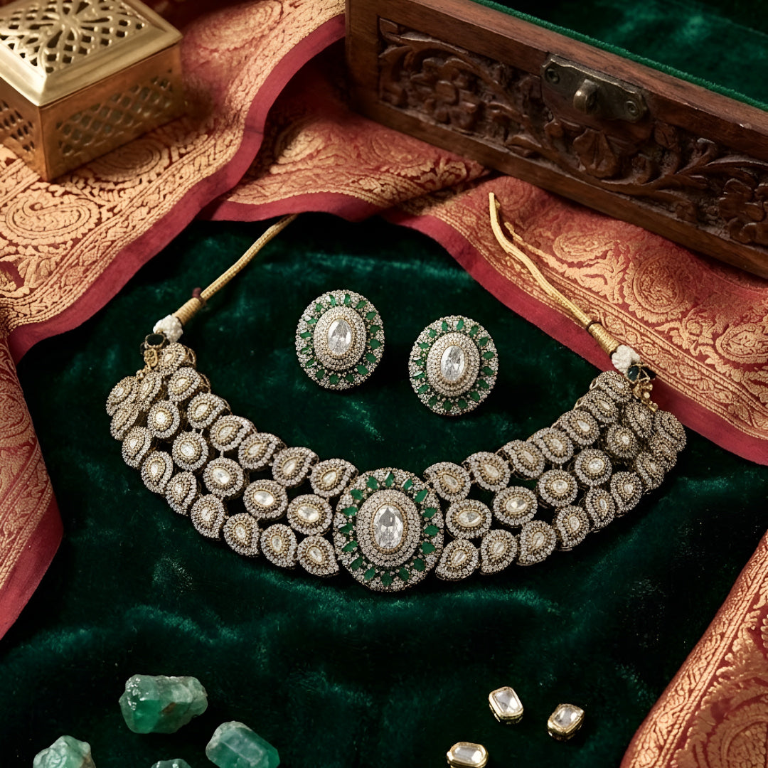 Elegant diamond and emerald choker necklace set with matching stud earrings featuring intricate floral motifs, sparkling white stones, green gemstone accents, and a luxurious gold-tone finish.