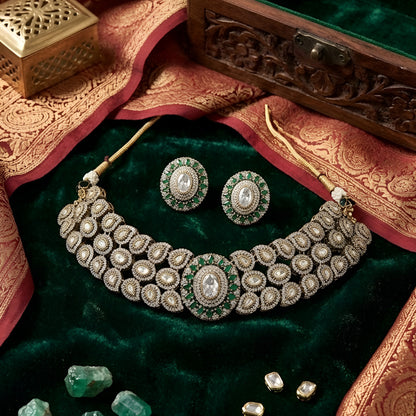 Elegant diamond and emerald choker necklace set with matching stud earrings featuring intricate floral motifs, sparkling white stones, green gemstone accents, and a luxurious gold-tone finish.