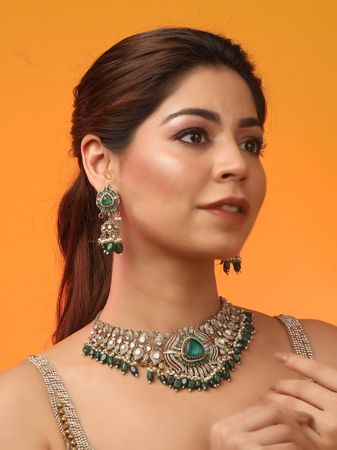 Detailed gold-toned statement necklace with intricate white stone embellishments and a prominent green teardrop centerpiece, finished with dangling green beads and pearls, paired with matching ornate drop earrings, displayed on a plain light background.