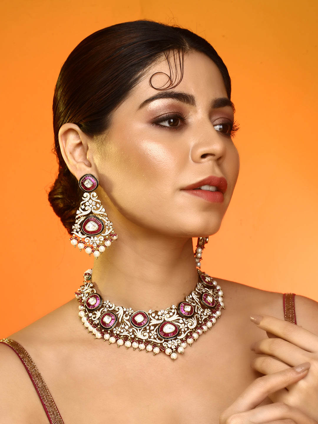 Gold-tone traditional necklace set with pink kundan-style stones, intricate detailing, pearl bead drops, and matching ornate dangling earrings.