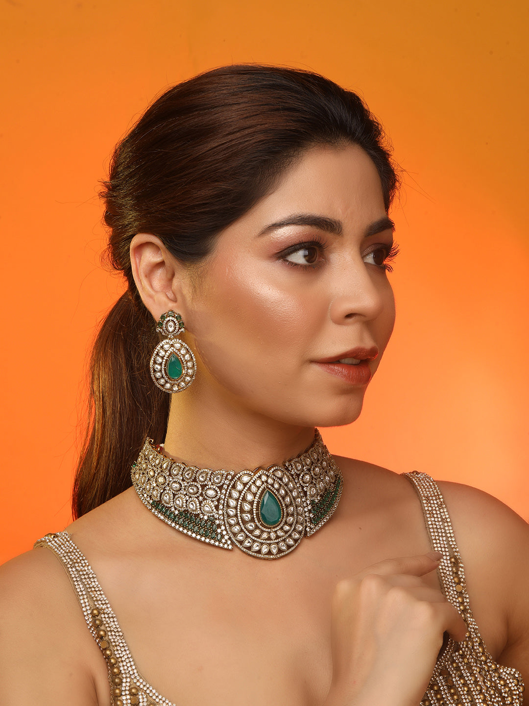 Gold-tone choker necklace set with intricate kundan-style detailing, highlighted by a large teardrop green stone centerpiece and matching drop earrings.
