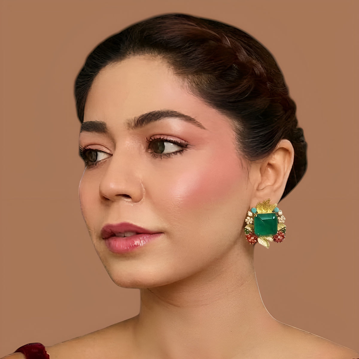 Pair of gold stud earrings with emerald-cut green centre stones, gold leaves, ruby-pink stone clusters, turquoise beads and pearls on a white background