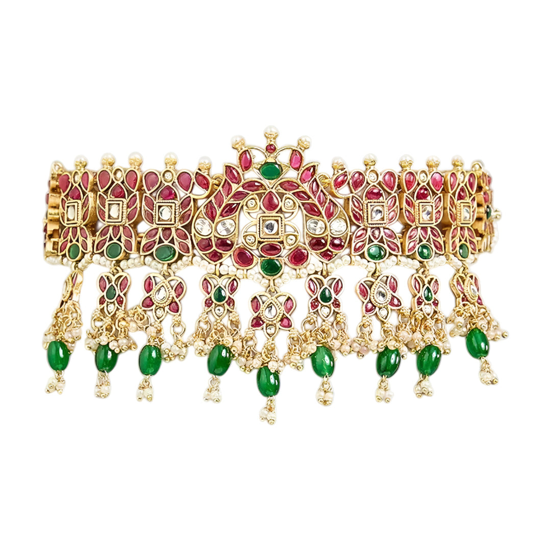 Traditional gold-plated Kundan choker necklace set with red and green stones, dangling green beads, and matching chandbali earrings for bridal wear.