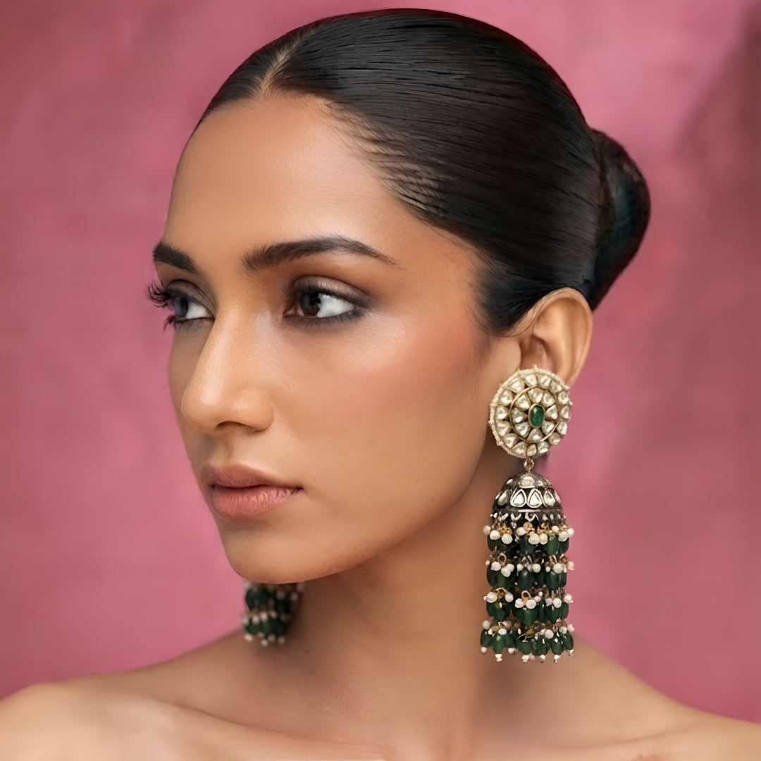 Green Kundan jhumka earrings with gold plating, emerald green center stone, pearl accents, and layered green bead tassels for bridal and festive wear.