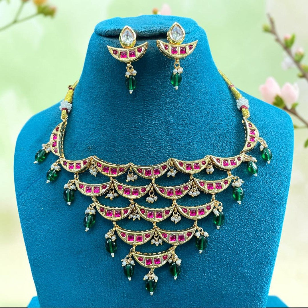 Gold-finish kundan crescent-tier necklace set with ruby-pink stones, green bead and pearl hangings and matching pear-top earrings
