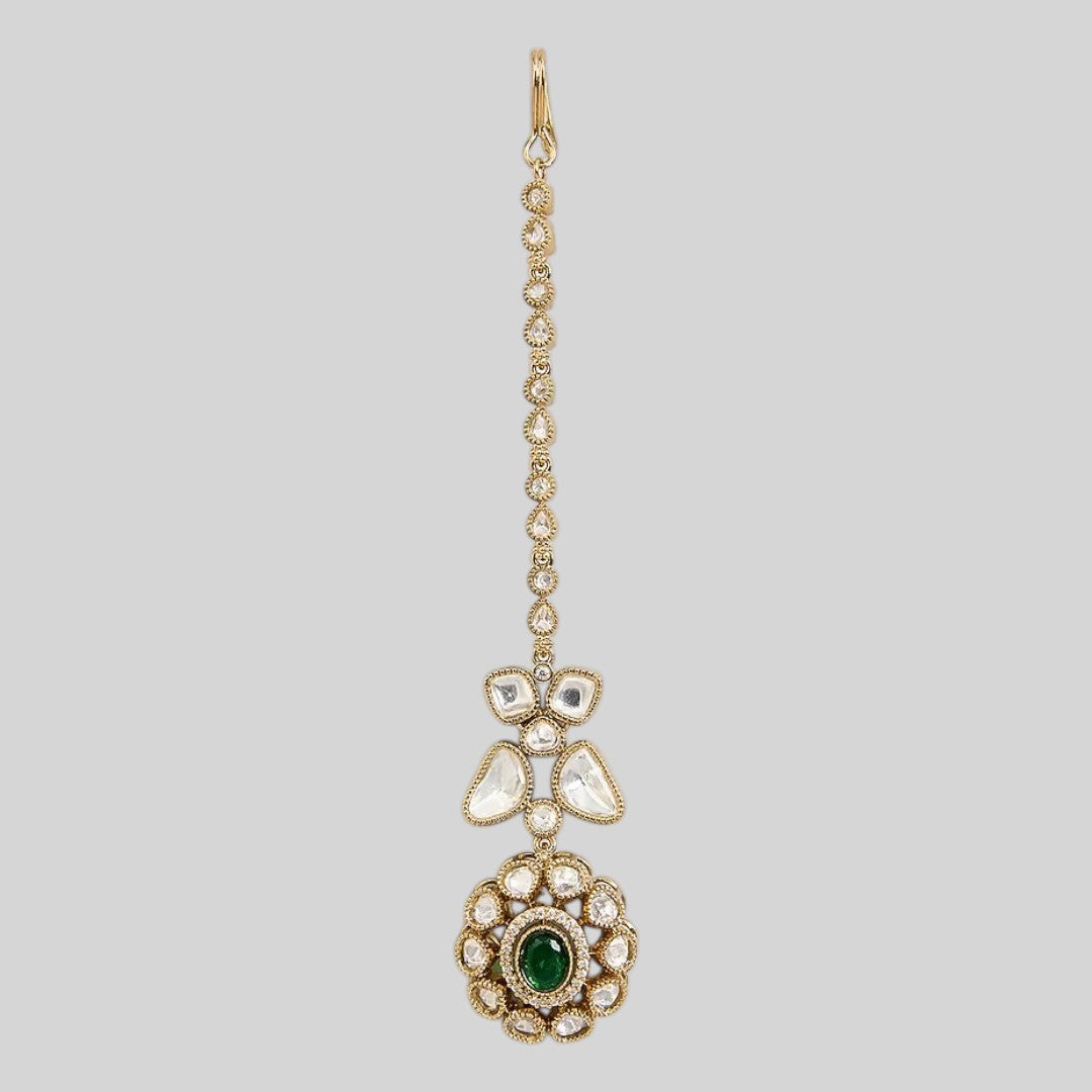 "Gold-toned maang tikka with polki clover motif and floral emerald-centered pendant, traditional Indian bridal jewelry"