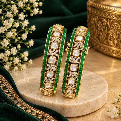 Pair of gold-finish openable kada bangles with emerald-green baguette stones, polki-style clear cushion-cut stones, and Victorian-style American diamond scrollwork
