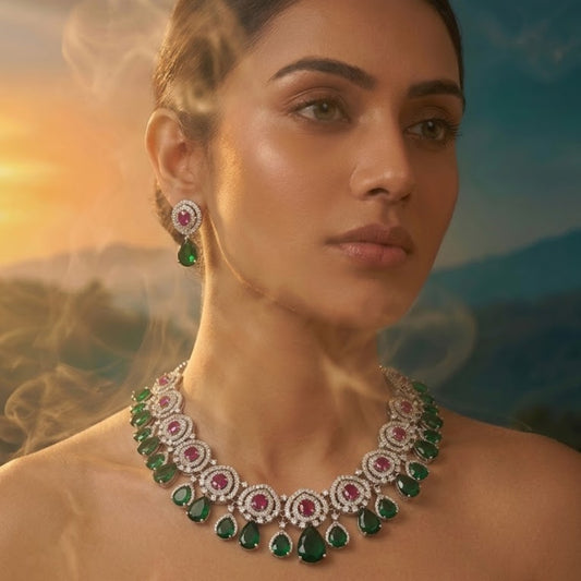 Luxury emerald green and ruby stone diamond-finish necklace set with matching earrings on white background.