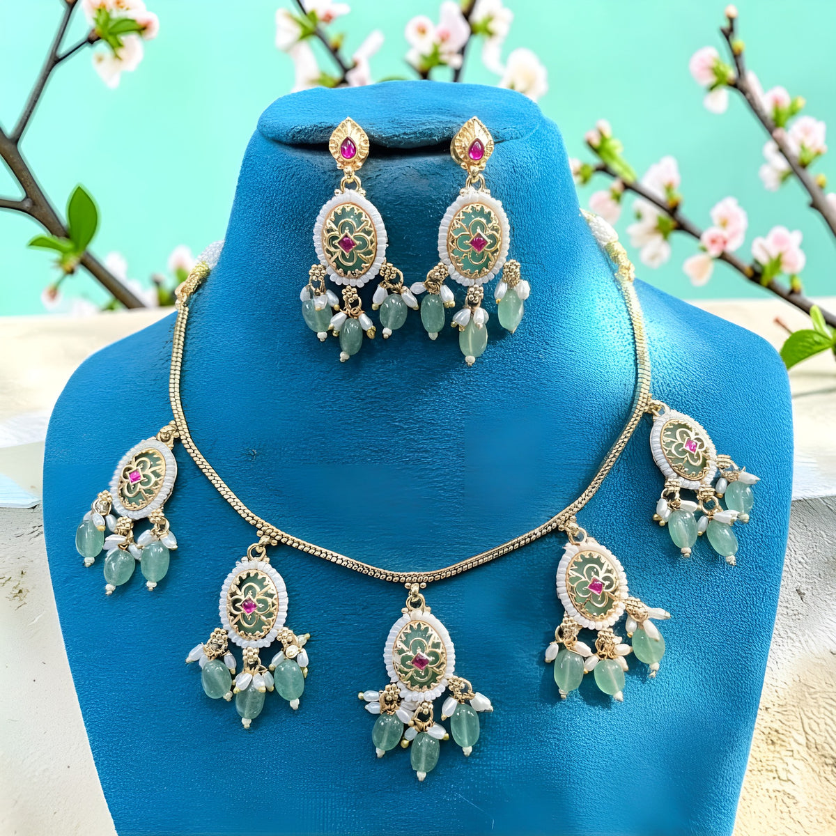 Gold plated mint green oval medallion necklace set with pink stones, green bead and pearl drops and matching earrings on a blue bust