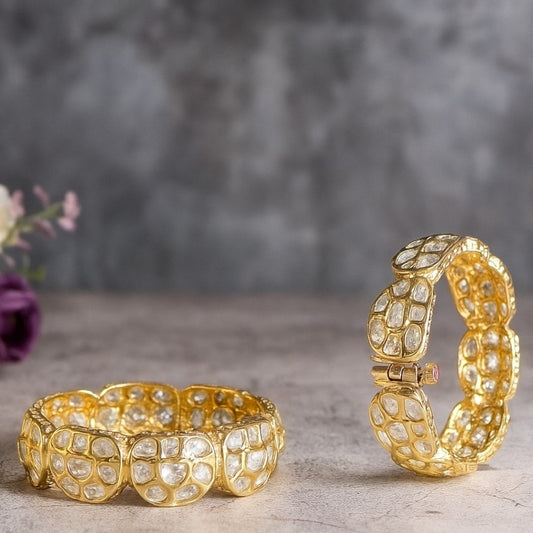 Gold plated traditional polki kundan bangles with petal-shaped panels, perfect for bridal and festive wear – displayed on a textured stone background with floral decor