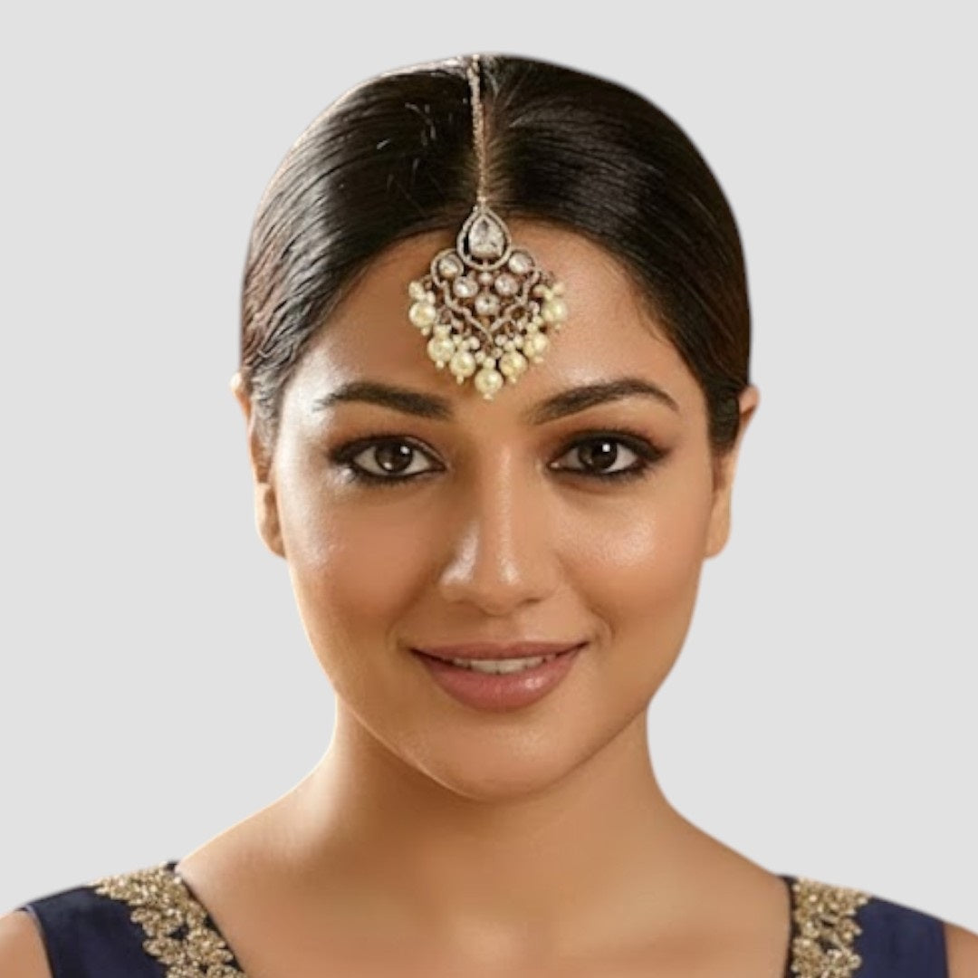 Gold-plated maang tikka with kundan stones and cream pearl danglers on a light background