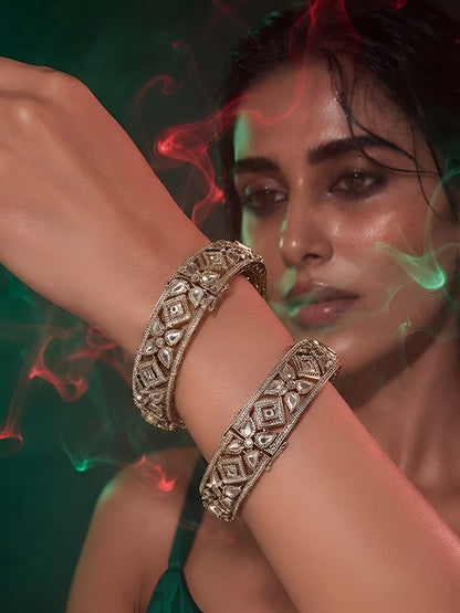 "Pair of gold-plated Kundan bangles with white stones in floral geometric design, traditional Indian bridal jewelry on white background"