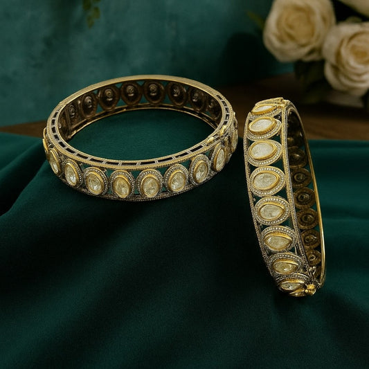 "Antique gold-plated bangles with oval polki stones in traditional Kundan style, placed on a green velvet cloth with floral background"