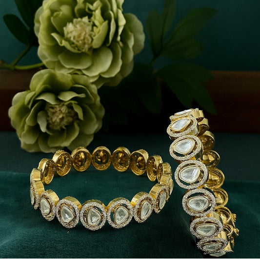 "Gold-plated bangles with teardrop Polki stones and micro-crystal detailing, displayed on green velvet with floral background"