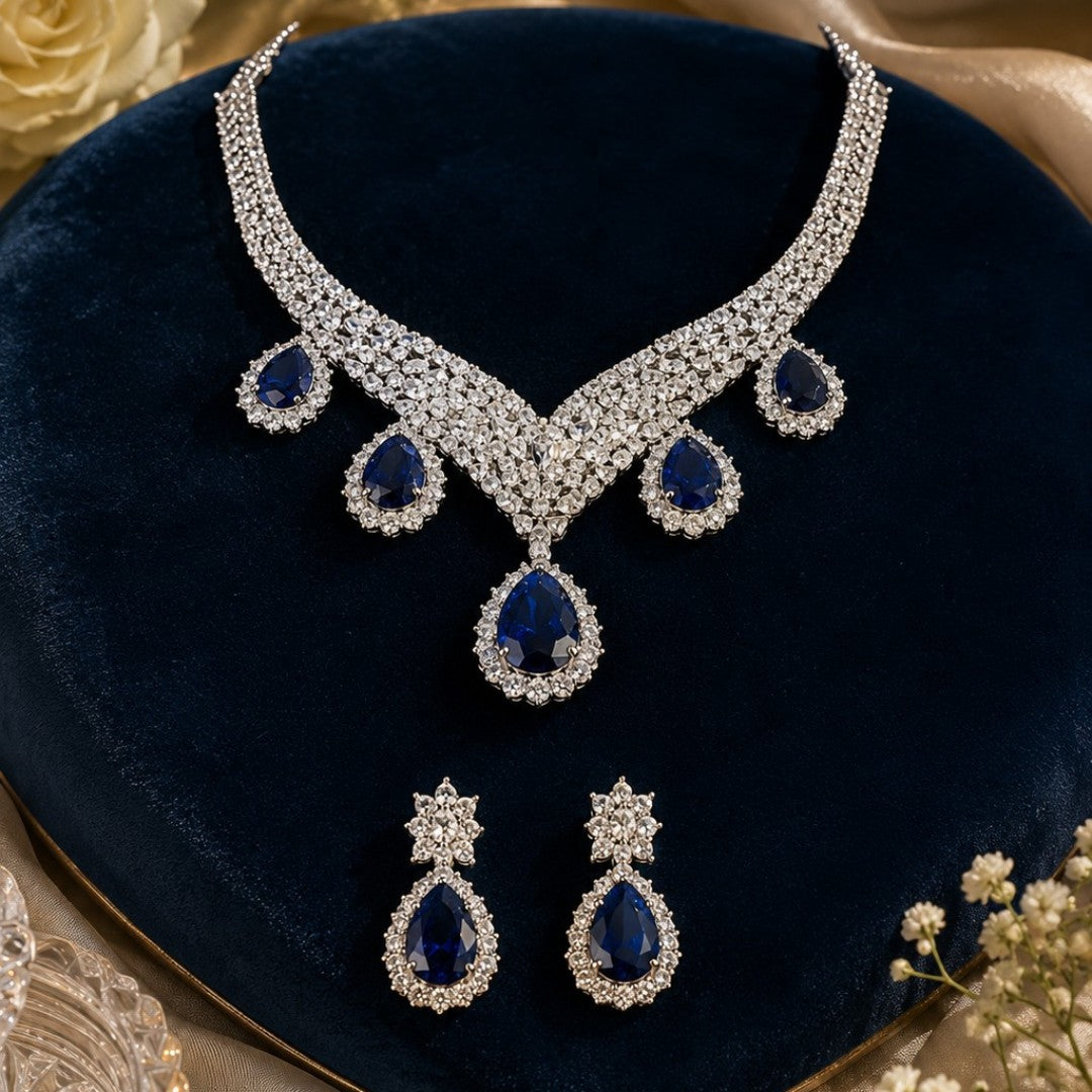 "Silver rhodium-plated V-shaped necklace set with white American diamonds and blue sapphire pear-drop stones, paired with matching teardrop earrings"