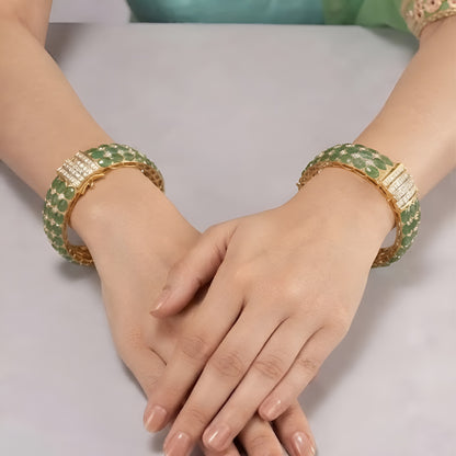 Pair of gold-plated Victorian style emerald green kada bangles with oval green stones, zircon pavé accents, baguette clasp panel and open lattice inner side